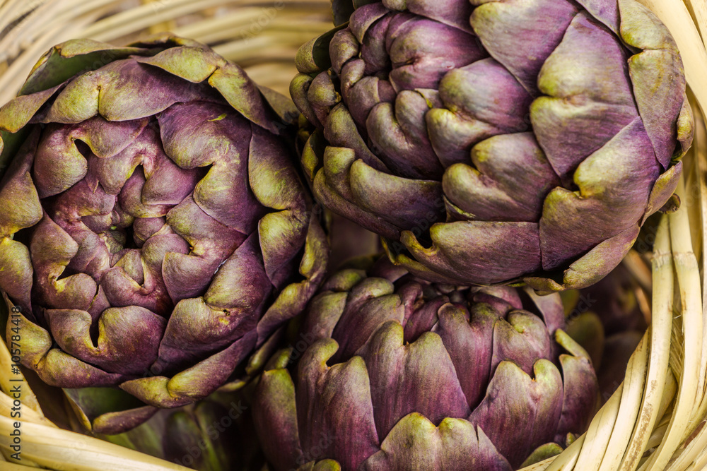 Fototapeta premium Fresh purple artichokes in wicker basket closeup background