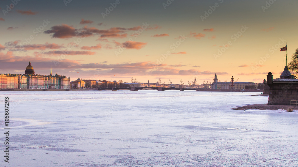Russia, Saint-Petersburg, 19 March 2016: The water area of ​​the Neva River at sunset, the Winter Palace, Palace Bridge, the dome of St. Isaac's Cathedral, pink clouds, frozen river