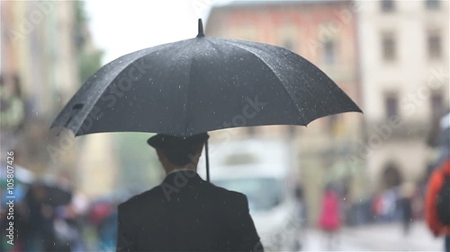 Stylish man in hat walks with umbrella on rainy street. Back view photo