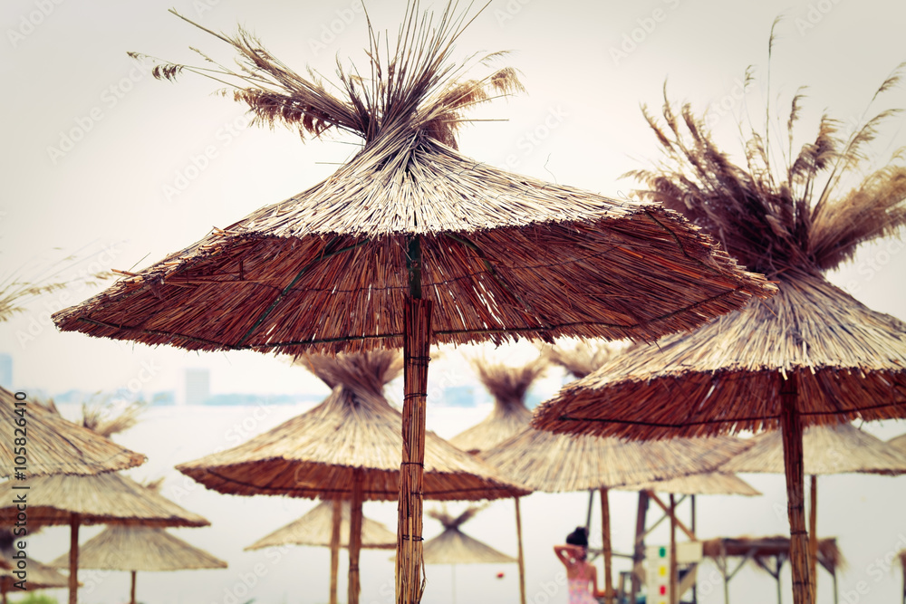 Beach sunshade parasols made of dried straw. Straw beach umbrellas. Toned image. Shallow depth of field. Selective focus.