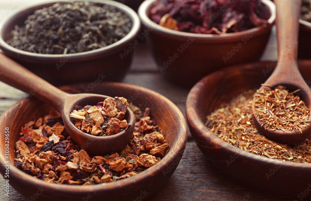 Variety of tea in clay bowls with spoon on wooden table, close up Variety of tea in clay bowls with spoon on wooden table, close up