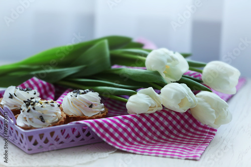 Fototapeta Naklejka Na Ścianę i Meble -  White spring tulips and delicious cupcakes in a purple tray covered with checkered napkin on a white table, close up