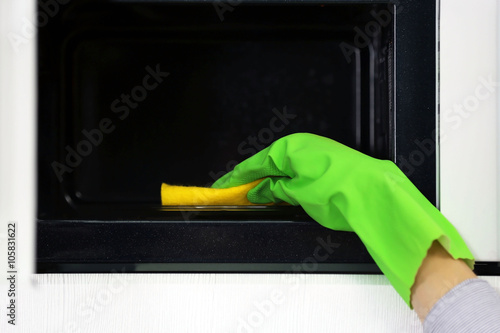 Female hand cleaning microwave with a sponge