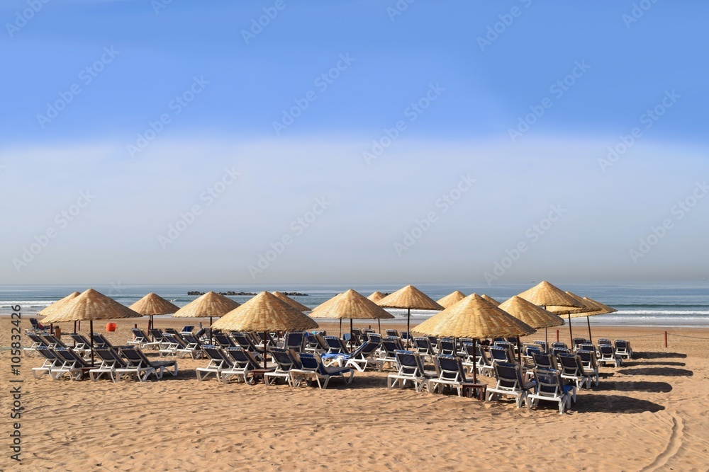 Sonnenliegen und Sonnenschirme warten aufgerreiht am Strand auf Sonnenanbeter Sonnenliegen und Sonnenschirme warten aufgerreiht am Strand auf Sonnenanbeter