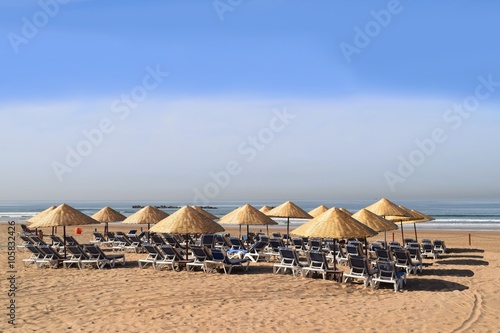 Sonnenliegen und Sonnenschirme warten aufgerreiht am Strand auf Sonnenanbeter © ArndtLow