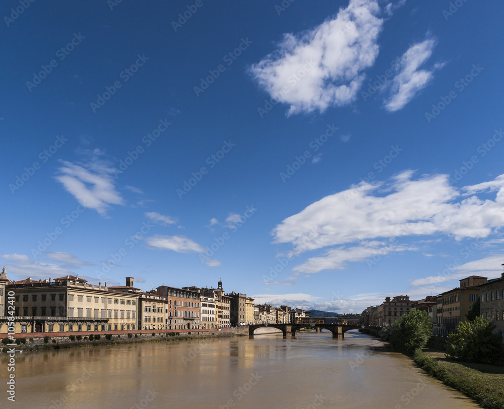 Summer Sky over the Arno River: A bright blue sky with a few white clouds over the yellow Arno river in Florence, Italy