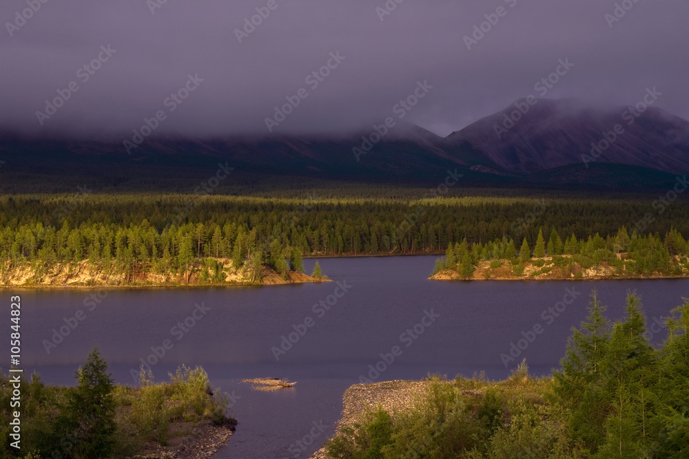 Lakeside in sunset light and low clouds in the mountains. Lake Darpir. Yakutia. Russia.