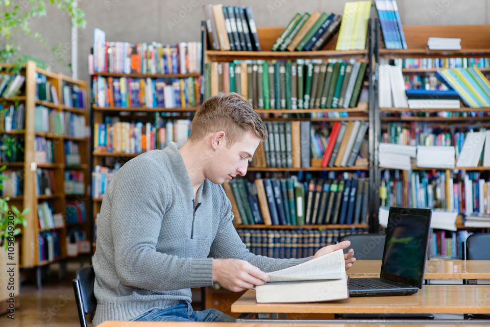Male student with laptop studying in the university library Male student with laptop studying in the university library