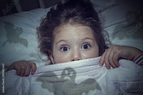 Foto scared cute little girl under the blanket in her bed