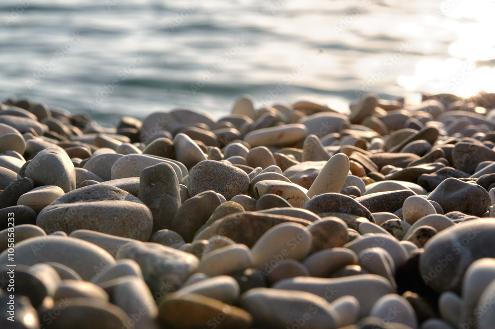 Obraz premium Sea gravel shore or beach with sea water at sunset