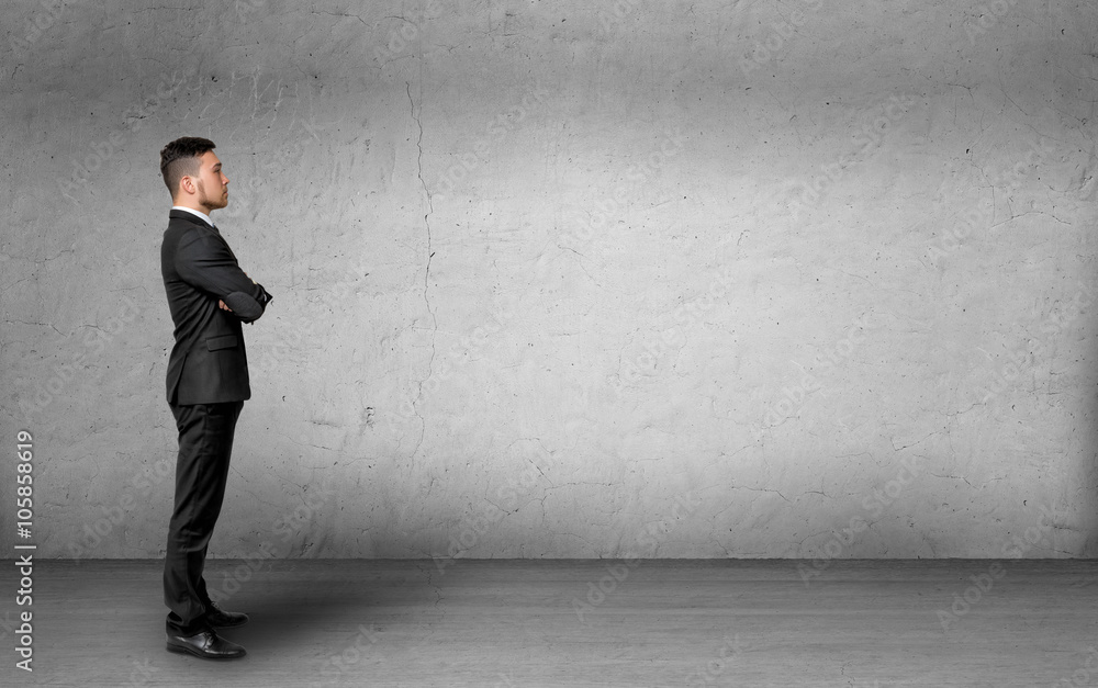 Young man in business suit, standing front of the concrete wall background. Business concept Young man in business suit, standing front of the concrete wall background. Business concept