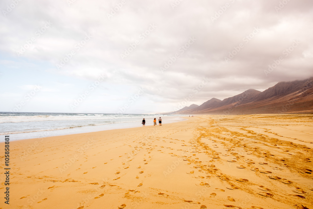 Cofete beach with people walking at the cloudy and foggy weather on Fuerteventura island in Spain Cofete beach with people walking at the cloudy and foggy weather on Fuerteventura island in Spain