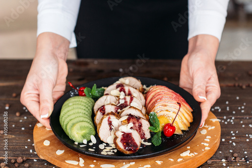 Waiter serving a baked veal with fresh fruits and sweet  sauce . Waiter serving baked veal for retail. Chief decorating food for presentation in restaurant. 