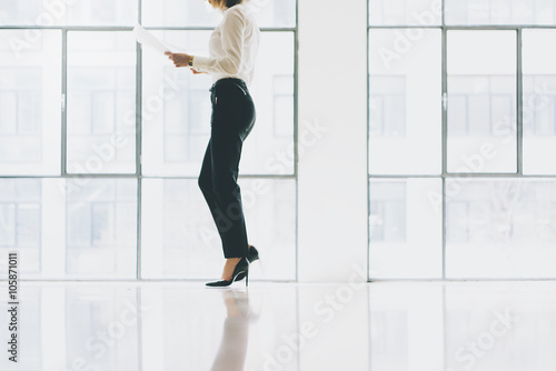 Closeup photo business woman wearing suit. Open space loft office. Holding papers hands. Analyze plans, meeting, panoramic windows background. Horizontal mockup.