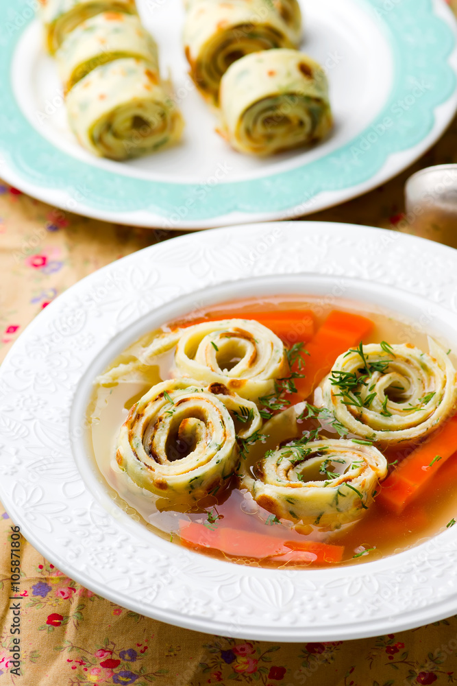 Broth with pancakes and carrots in a white plate.