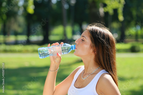  young beautiful brunette woman drinking a water from bottle in a park