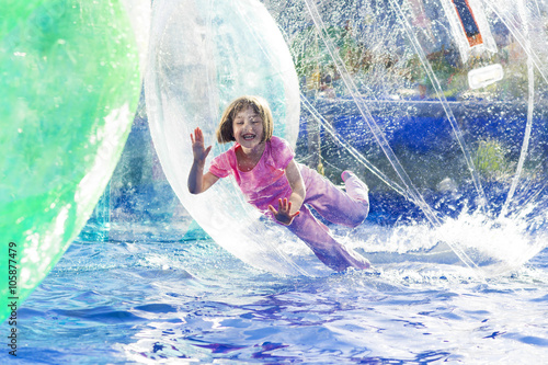 Young girl playing inside a floating water walking ball. © fotoyou
