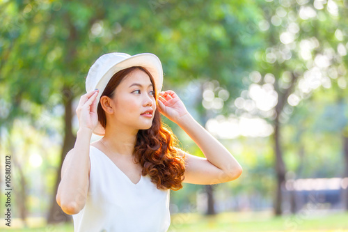 Portrait of pretty cheerful woman wearing white dress and straw hat in sunny warm weather day. Walking at summer park and smiling