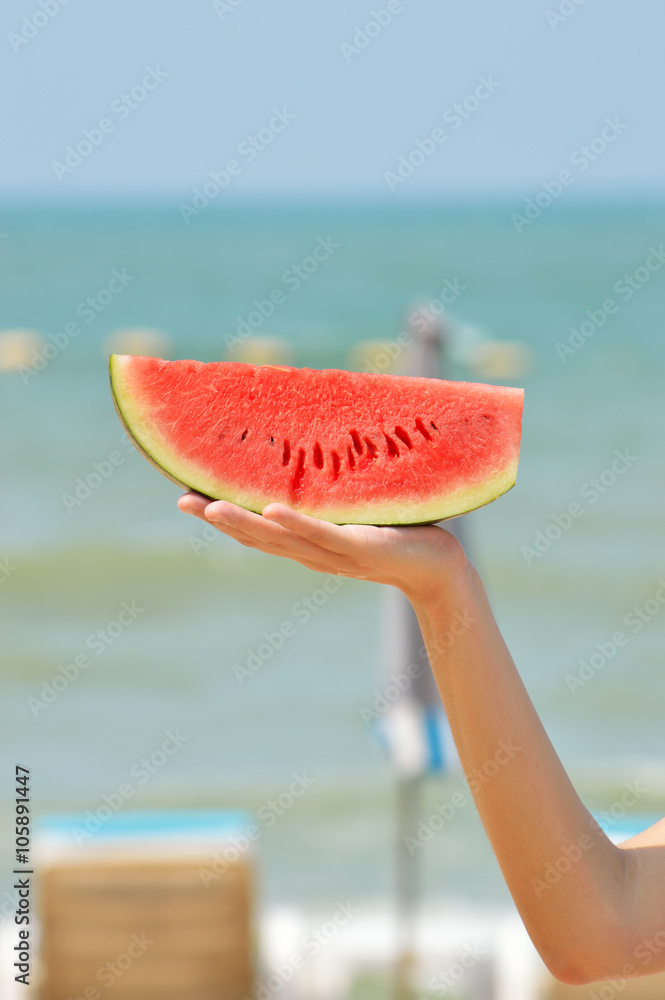 Hand with slice of watermelon on beach background Hand with slice of watermelon on beach background