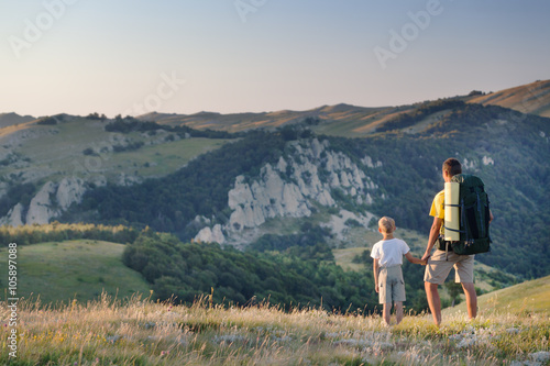 Man and young boy standing in a mountain meadow. 