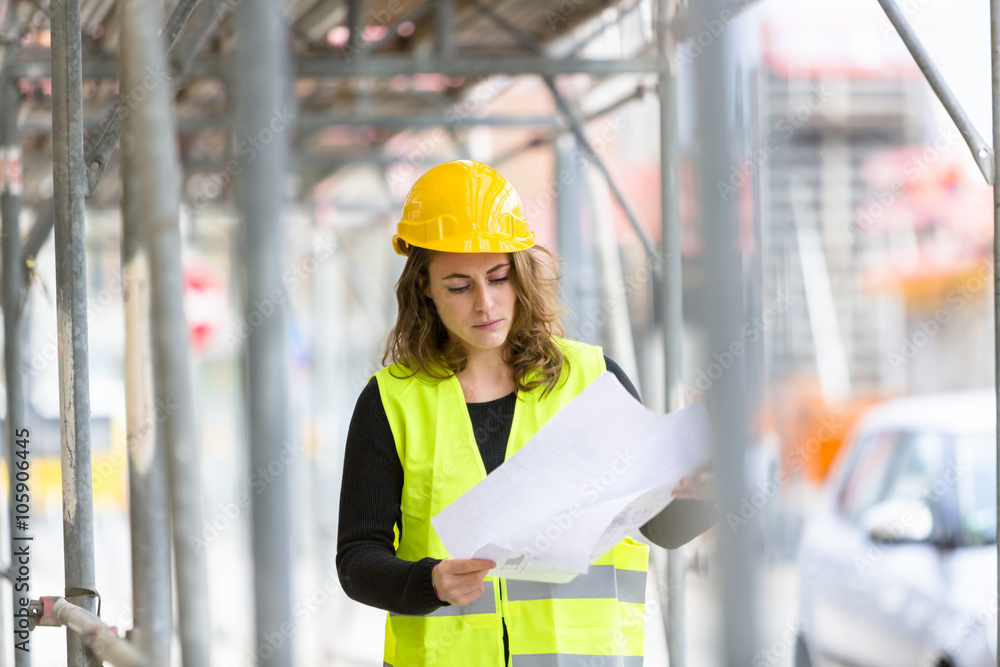 Female engineer with helmet and safety jacket on construction site examining office blueprints. Outdoors Female engineer with helmet and safety jacket on construction site examining office blueprints. Outdoors
