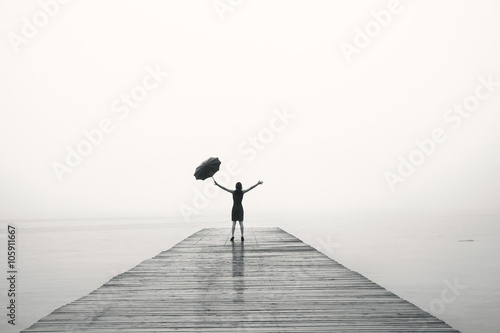 elegant woman in black rejoices with their arms up in the rain