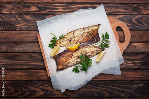 Grilled fish with herbs and lemon on rustic dark wooden background