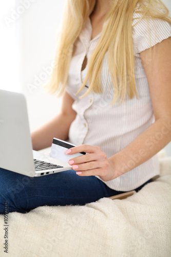 Happy woman doing online shopping at home . Close- up of a hand holding a credit card next to a laptop