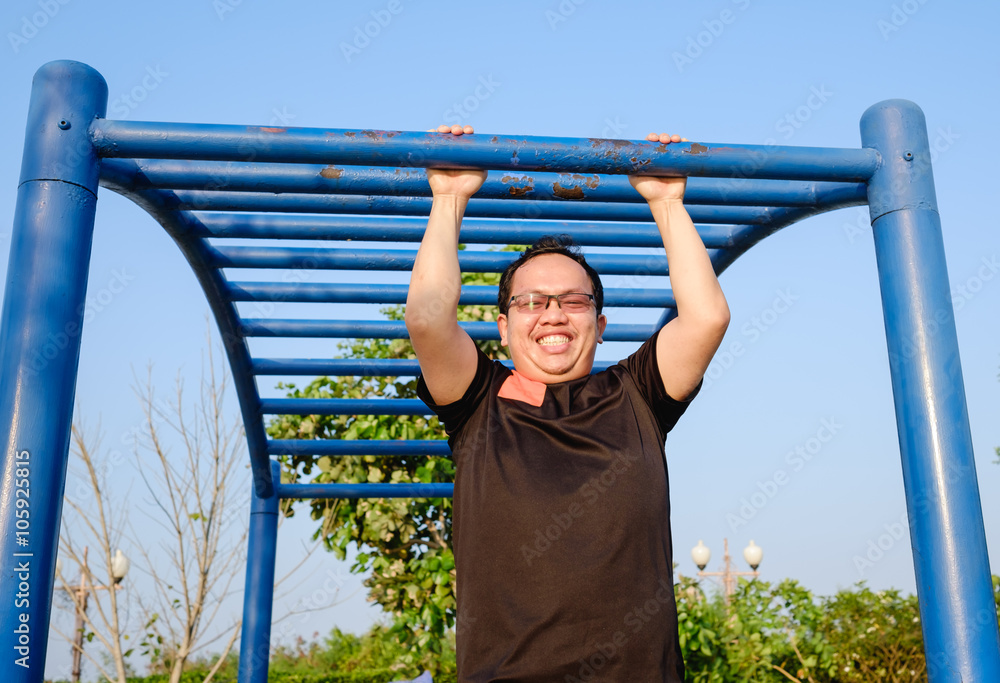 Fototapeta premium fitness ,sport, exercise, training and lifestyle concept - one young adult fat man doing pull ups on horizontal bar outdoors