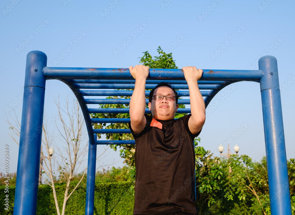 Fototapeta premium fitness ,sport, exercise, training and lifestyle concept - one young adult fat man doing pull ups on horizontal bar outdoors