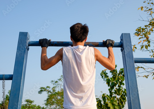 fitness ,sport, exercise, training and lifestyle concept - one young man doing pull ups on horizontal bar outdoors