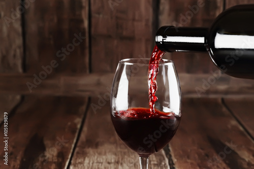 Red wine is pouring from a bottle into a glass