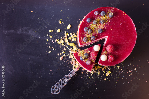 Delicious raspberry cake with fresh strawberries, raspberries, blueberry, currants and pistachios on wooden background. Free space for your text.