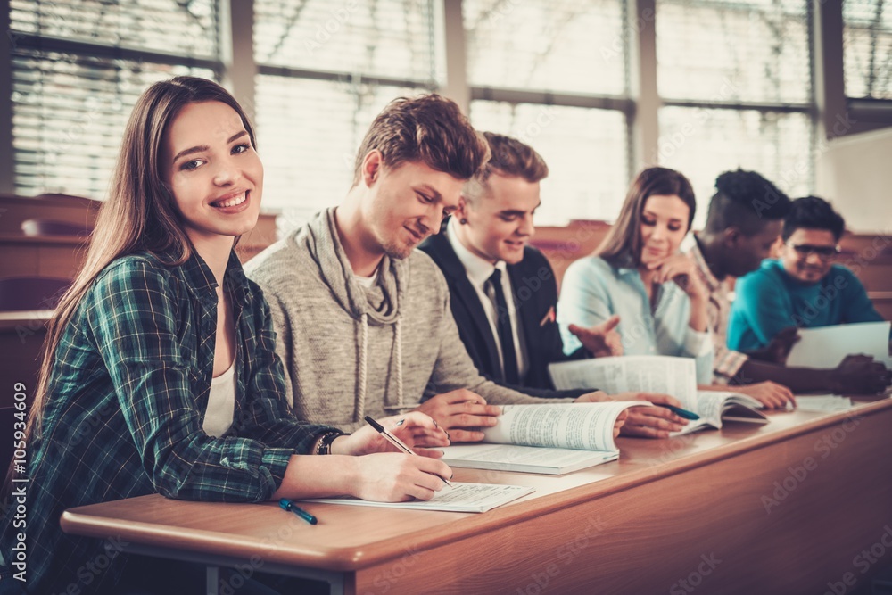 Multinational group of cheerful students taking an active part in a lesson while sitting in a lecture hall. Multinational group of cheerful students taking an active part in a lesson while sitting in a lecture hall.