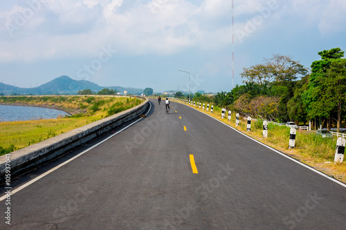 Cyclist riding bicycle on the road along water reservoir in Thailand