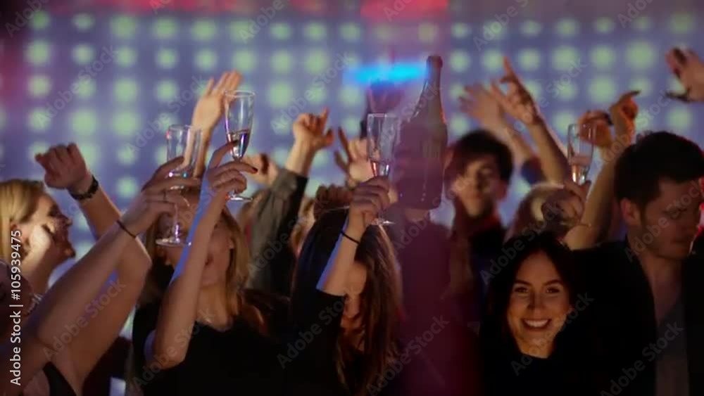 young people on dancefloor at club putting champagne glasses up in the air young people on dancefloor at club putting champagne glasses up in the air