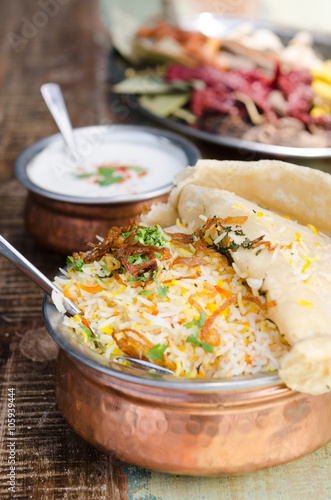 Authentic chicken biryani served with naan bread, fragrant pilau rice and yoghurt, in a metal pot. photo