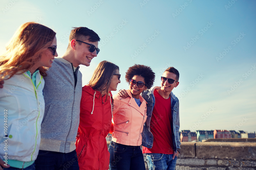 happy teenage friends walking along city street