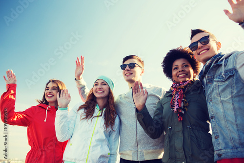 happy teenage friends in shades waving hands