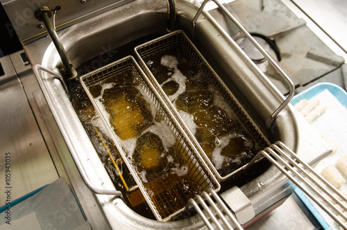 A silver deep pan industrial kitchen oil fryer, with golden oil, bubbling and frying potatoes