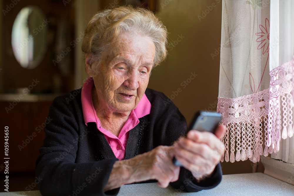 Elderly woman sitting at table typing on a smartphone. Elderly woman sitting at table typing on a smartphone.