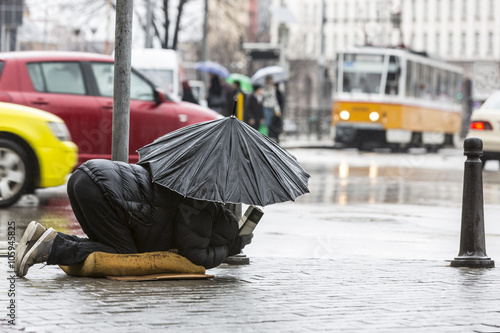 Foto Beggar in the rain with umbrella traffic