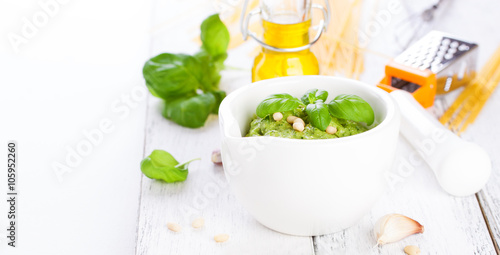 Homemade traditional basil pesto with olive oil, cedar nuts and garlic in a white bowl on a wooden rustic table on a white background with copy space or place for text, closeup
