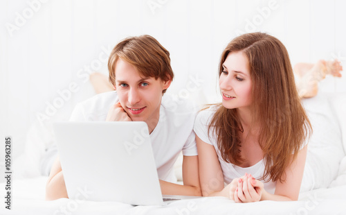 happy couple with laptop on internet in bed