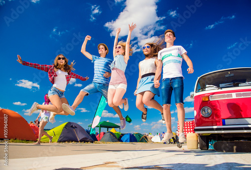 Teenagers at summer festival jumping by vintage red campervan