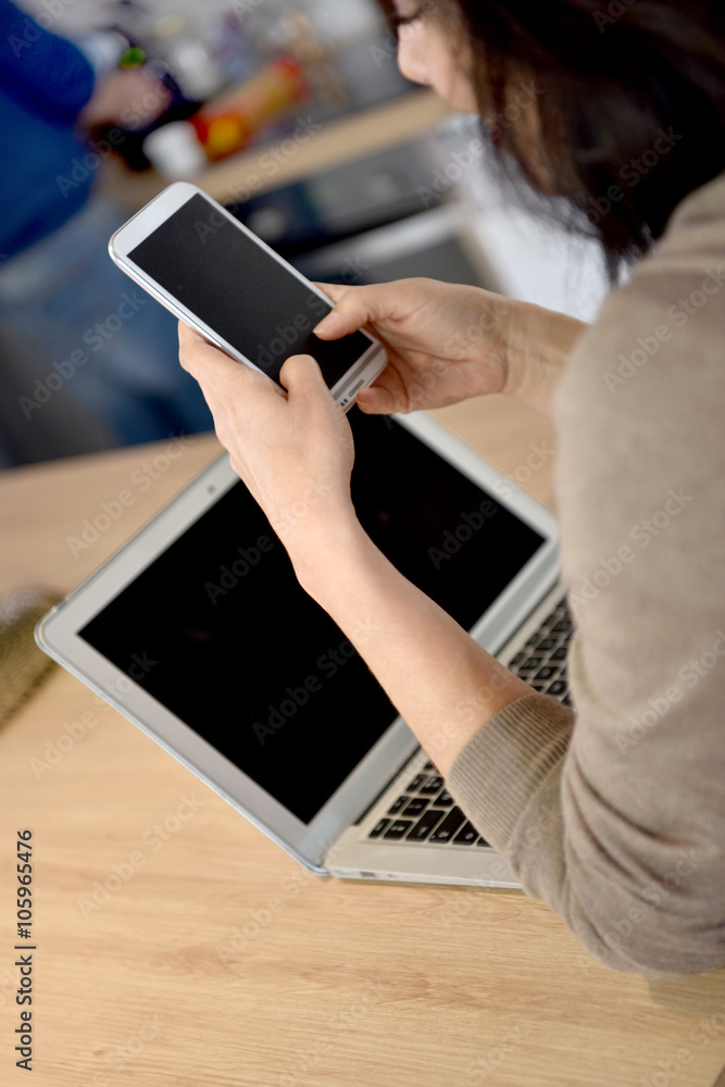 Back view of woman connected on smartphone and laptop Back view of woman connected on smartphone and laptop