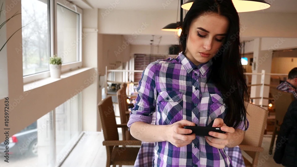 Young girl standing in the restaurand and using her mobile phone. 