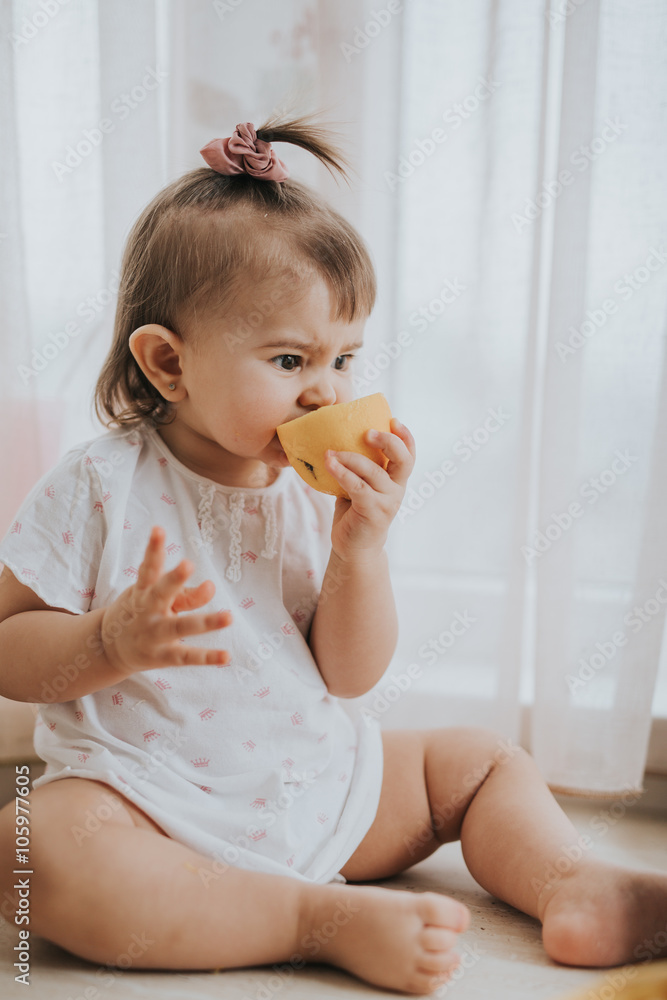Cute little baby girl on the table in the kitchen eats citrus fruits full of vitamins and makes funny cute faces Cute little baby girl on the table in the kitchen eats citrus fruits full of vitamins and makes funny cute faces