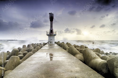 abandon beacon light tower with concrete break water surrounded by sea water and blur sunrise background.