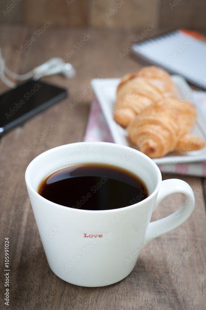 dining table with hot coffee cup and croissant, office equipment on wooden floor. dining table with hot coffee cup and croissant, office equipment on wooden floor.